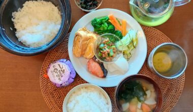 A Japanese breakfast: white rice, vegetable miso soup, tamagoyaki (omelet), salted grilled salmon, boiled vegetable salad, and pickled Chinese cabbage and turnip with kelp and yuzu salt. Toppings include shiso-flavored nori and turnip leaf furikake (with bonito flakes, soy sauce, sesame oil).